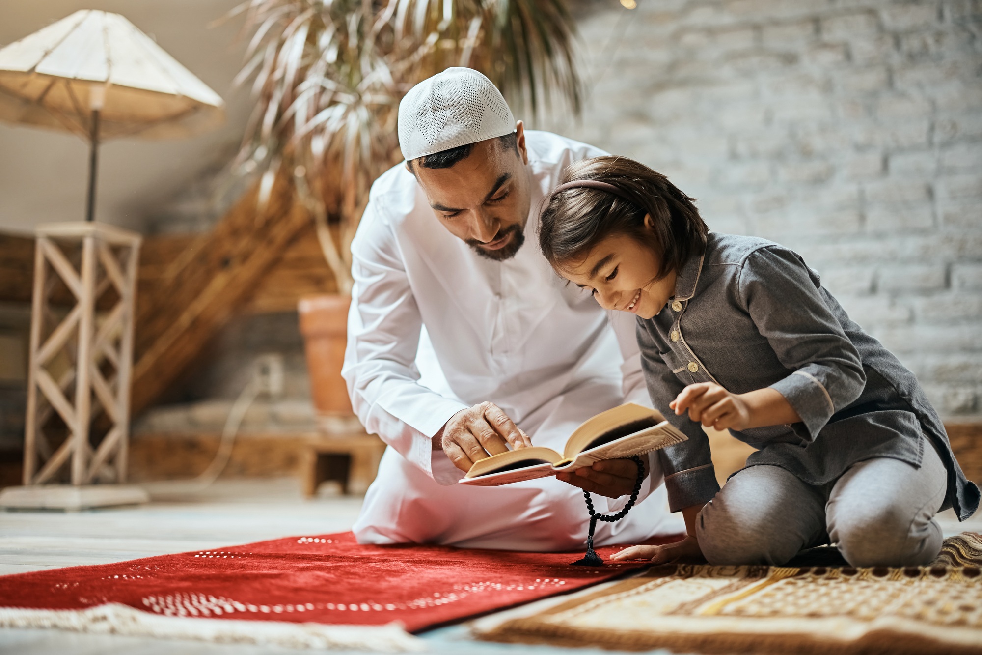 Happy Muslim girl and her father reading Koran at home.