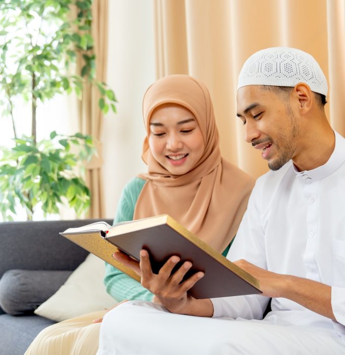 Side view of couple muslim man and woman sit on sofa and read islam teaching book together