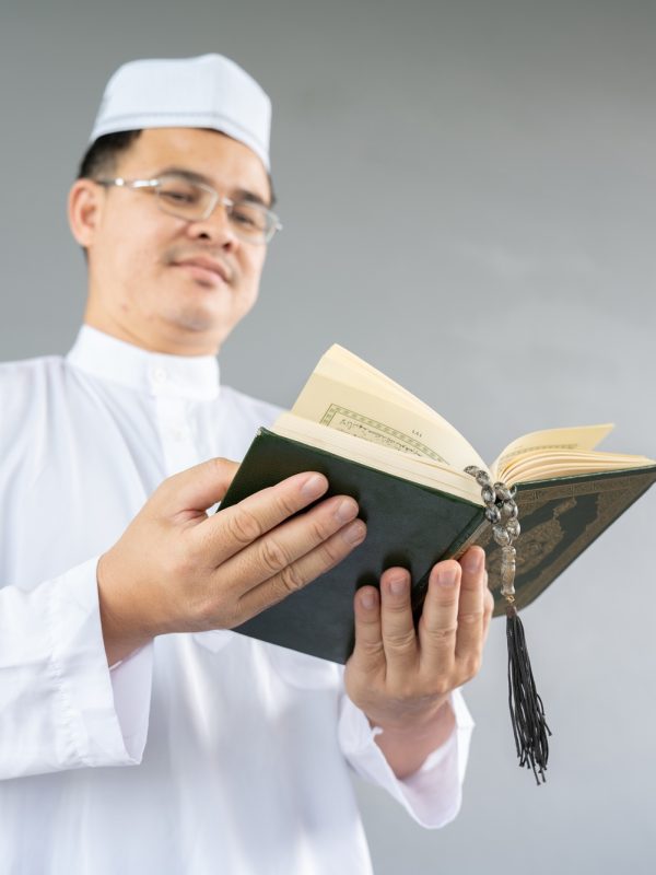 Muslim man reading a book on gray background, in Islam study. Hand of muslim