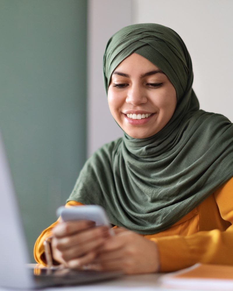 Portrait Of Beautiful Young Arab Woman In Hijab Using Smartphone In Office