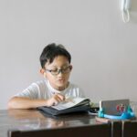 Asian kid reading Al-Quran through video call using smartphone during education and learning from ho