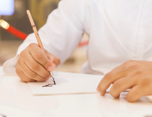 man-creating-calligraphy-art-on-a-white-piece-of-paper-hands-in-frame