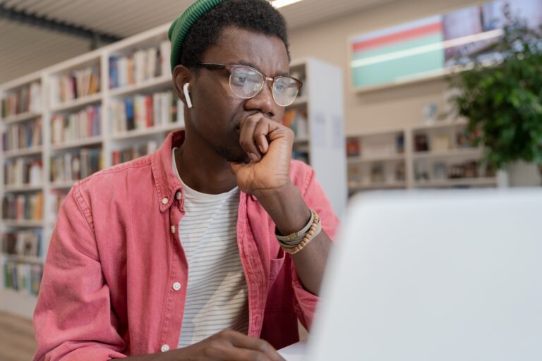 focused-african-american-student-guy-watching-online-course-on-laptop-in-library