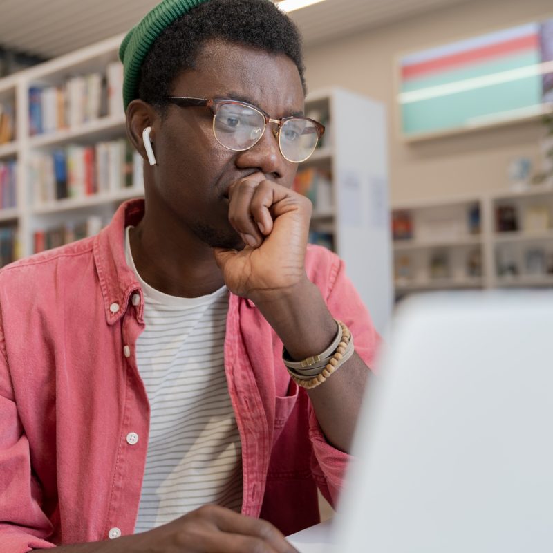 focused-african-american-student-guy-watching-online-course-on-laptop-in-library
