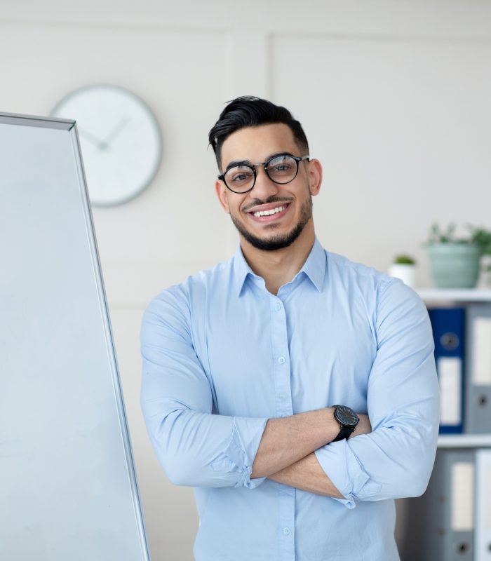 online-learning-during-covid-friendly-arab-teacher-posing-near-empty-blackboard-with-crossed-arms
