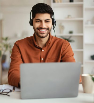 arab-man-using-laptop-wearing-headset-sitting-at-desk