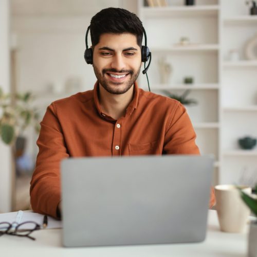 arab-man-using-laptop-wearing-headset-sitting-at-desk