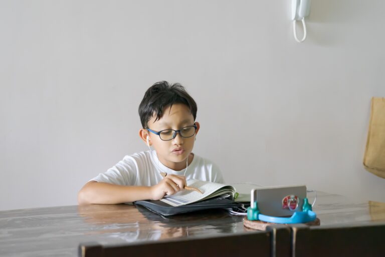 Asian kid reading Al-Quran through video call using smartphone during education and learning from ho