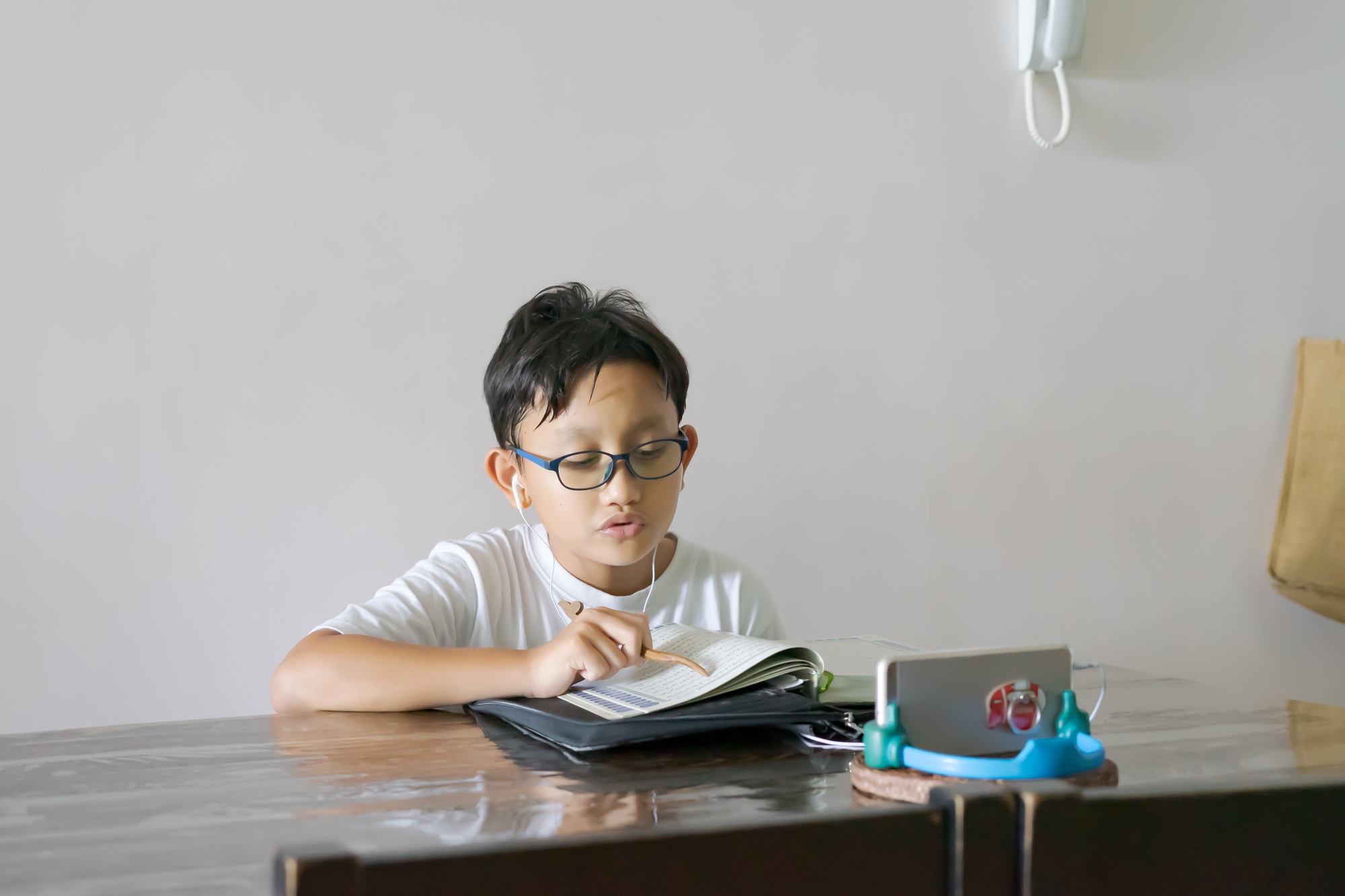 Asian kid reading Al-Quran through video call using smartphone during education and learning from ho
