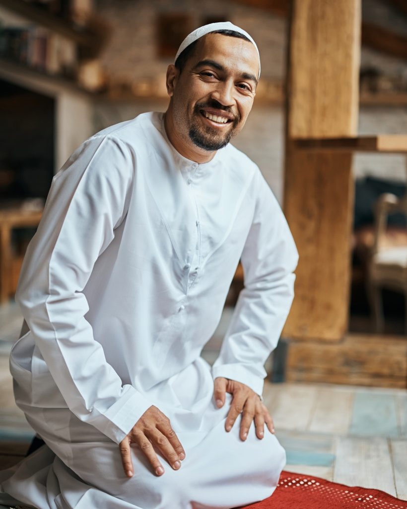 happy-muslim-on-kneeling-on-a-prayer-mat-at-home-and-looking-at-camera- (1)