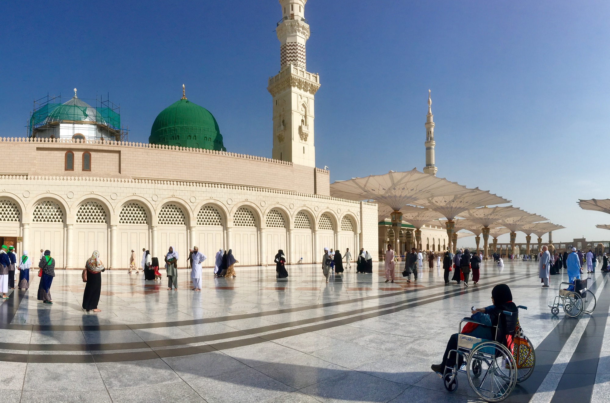 A pilgrim in wheelchair in foreground sits facing the Prophet’s Mosque in Madinah