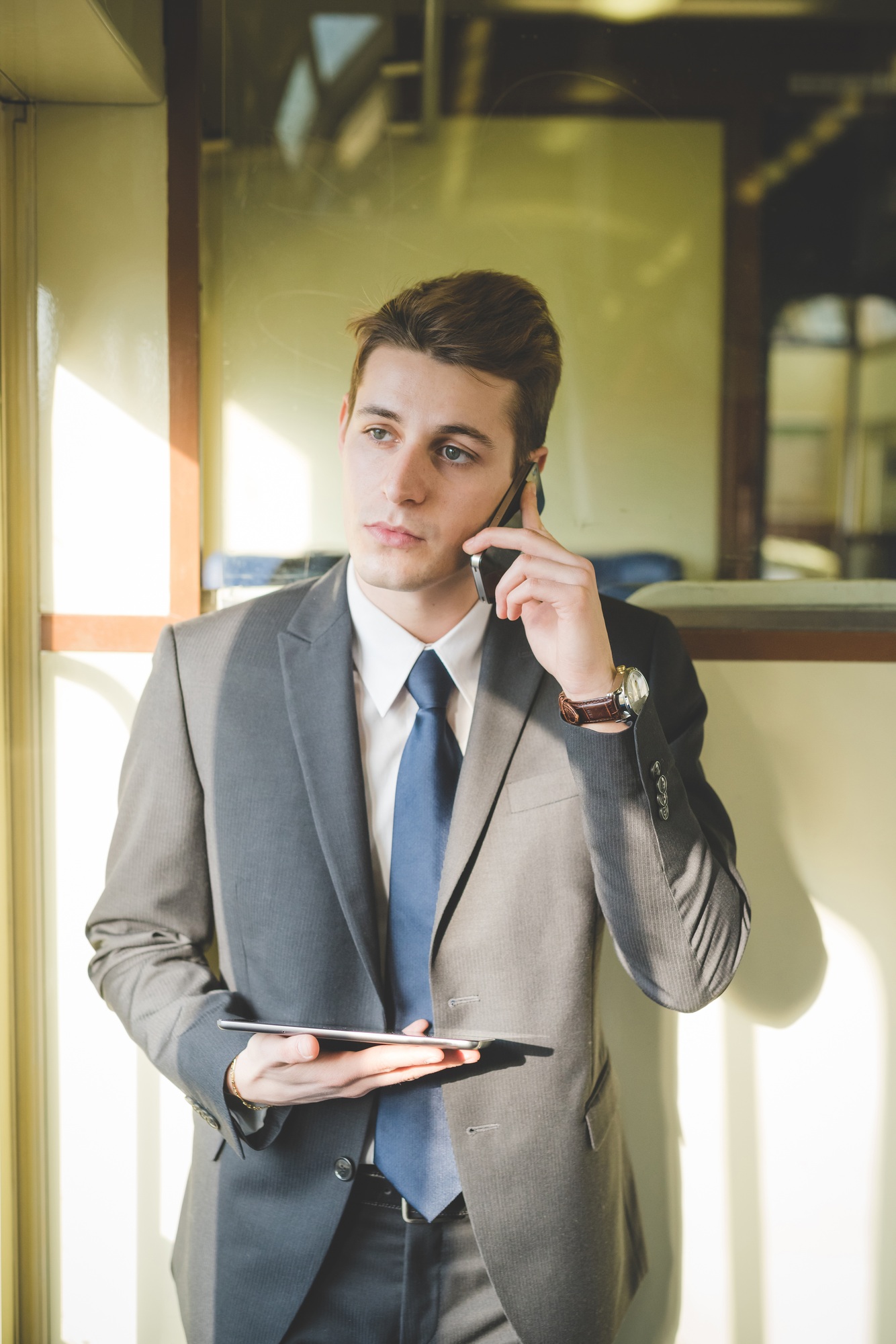 Portrait of young businessman commuter using digital tablet and smartphone on train.